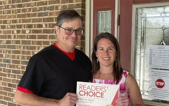 Dr. Rich McCurdy & Dr. Kate McCurdy holding a Readers’ Choice award while standing in front of a brick building.