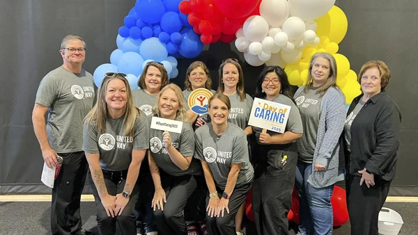 Team wearing matching shirts at a community event, posing together with colorful balloons.